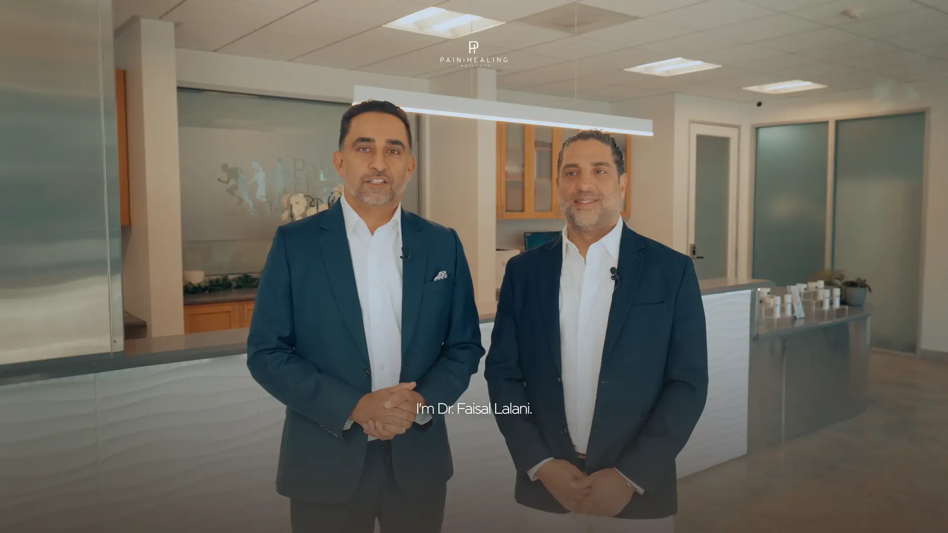 The two physicians at reception, the opening frame of the Pain & Healing brand film.