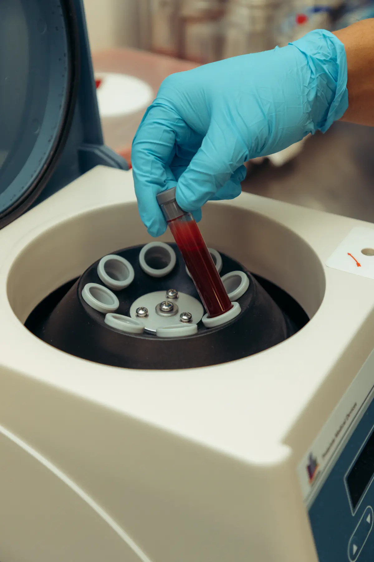 A gloved hand lifting a tube from the centrifuge.