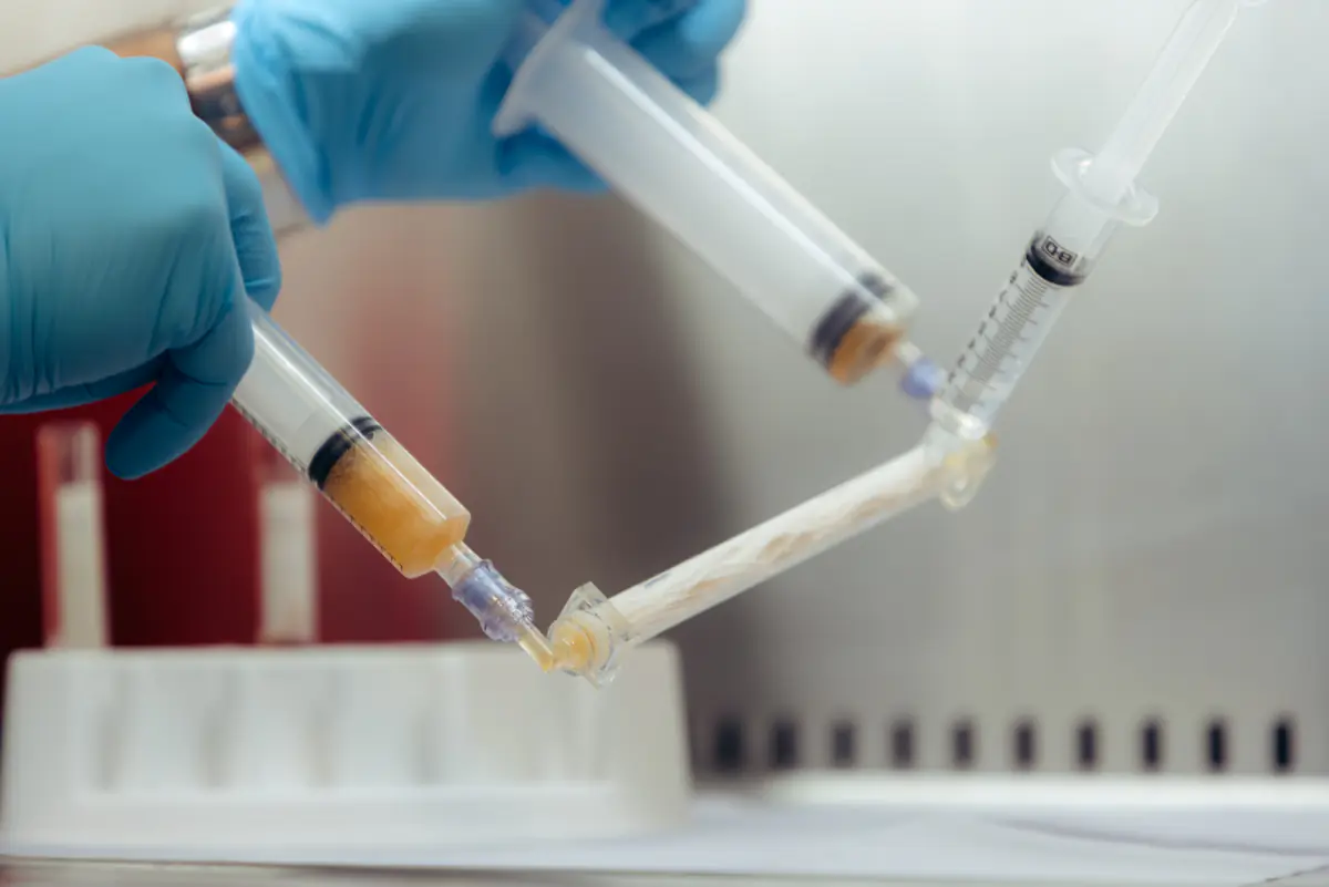 Gloved hands joining two syringes in the Pain & Healing Institute lab.