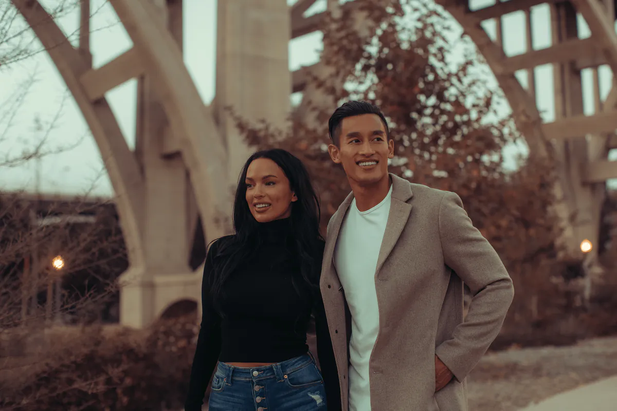 A couple in autumn coats beneath the arches of a concrete bridge.