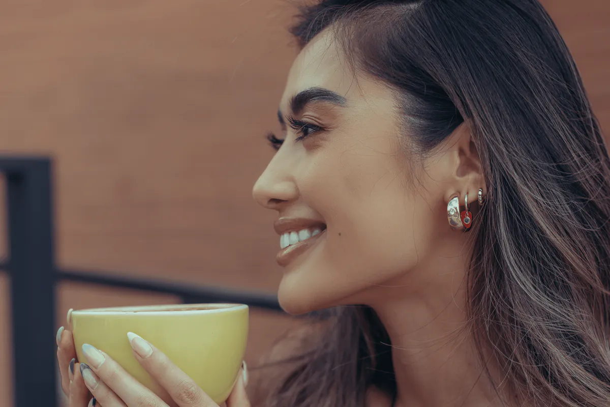 A woman in profile, smiling over a green cup.