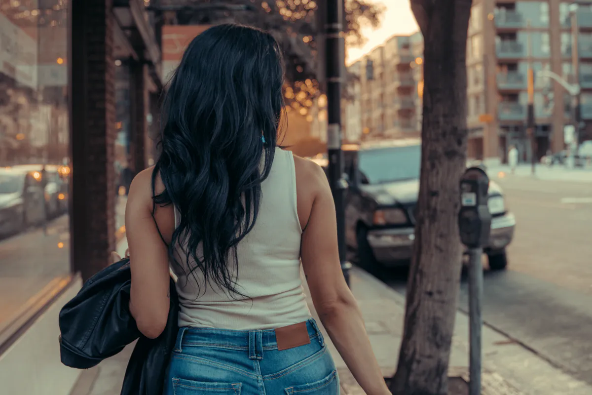 A woman walking away down a tree-lined city street.
