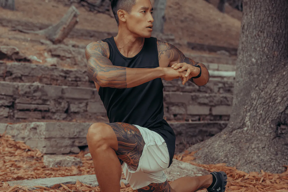 A man stretching on old stone steps under the trees.