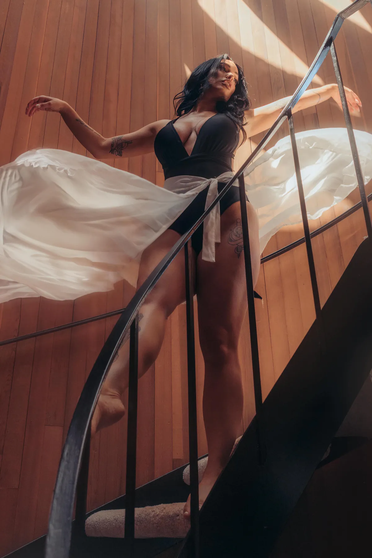 A woman on a spiral staircase, sheer fabric trailing in the light.